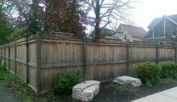 A few simple rocks and shrubs can break up the monotony of a large side yard privacy fence. This basic fence is dressed up slightly with top rail peak boards.