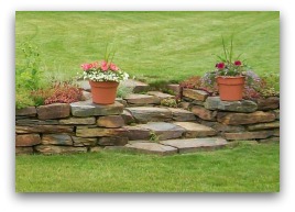 This low natural stone retaining wall with staircase creates interest in the yard by making the lawn space multi-level. Tiers or levels are a great way to deal with slopes.