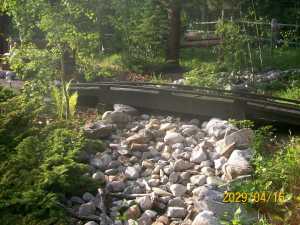 Dry river bed with footbridge in backyard.