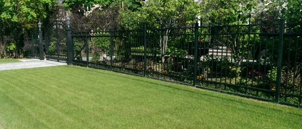 A tall wrought iron fence and front driveway security gate provide a barrier, but still leave an open view to the home and gardens.