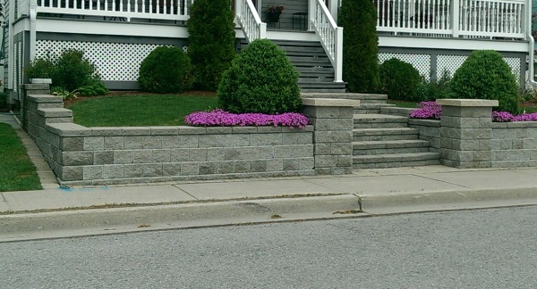 A stone block retaining wall and steps lead to the porch of this small sloped front yard.