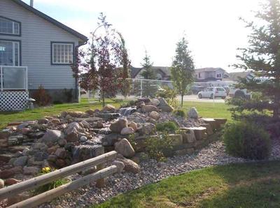 Add trees and shrubs around a built up water feature to balance the height in a flat yard.