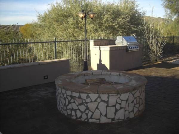 A mortared flagstone firepit sits centered in a large outdoor entertaining and kitchen area.