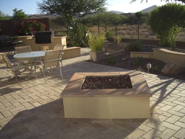 A square firepit is set off to one side of an outdoor kitchen area.