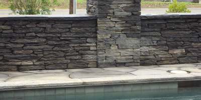 A poolside wall with a pillar are capped with flagstone