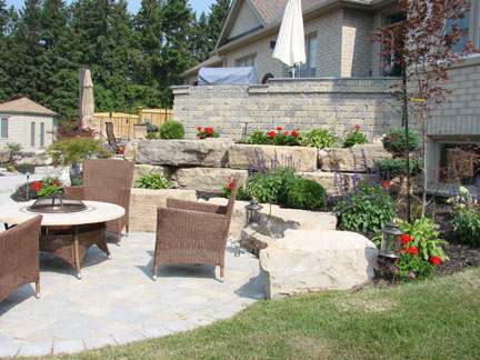 A patio with a firepit is complimented with a wall built out of very large stones.