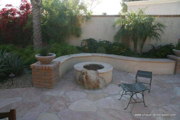 This creative little nook has blended many different materials like flagstone, brick, mortar, and even a boulder into the firepit wall itself