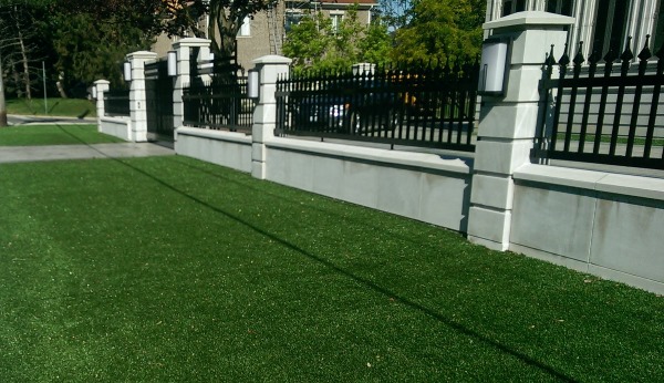 Security fencing and gates sitting on top of a concrete wall. This is artificial turf for lawn. (It has come a long way)