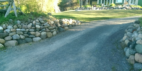Simple boulder walls line the entrance to this long driveway,  Boulders are an easy way to deal with slopes.