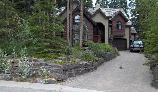 The stone walls and interlocking brick driveway used here are a great way to blend a design into the existing natural landscape.