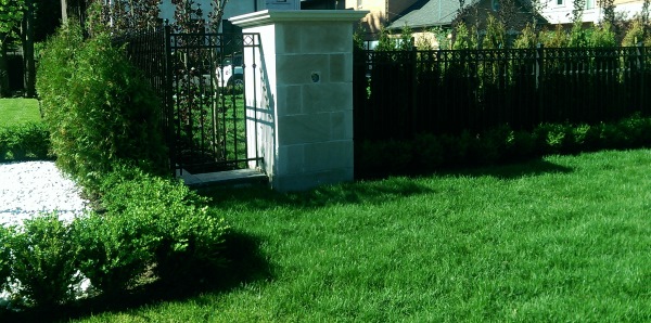 Iron fencing connected to large brick pillars lined with hedges for privacy.