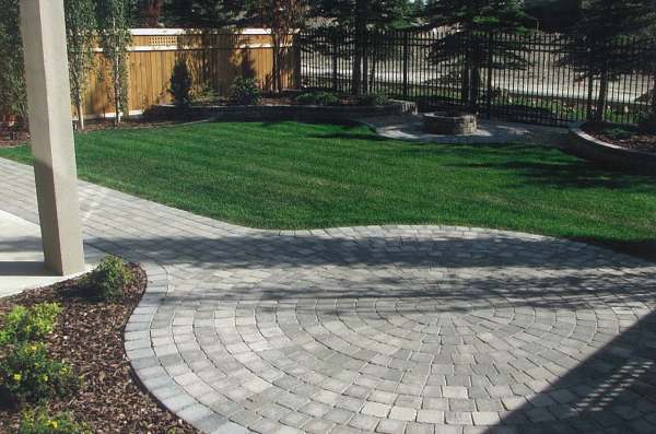 A nicely balanced backyard design with two raised corner beds separated by a small firepit area.