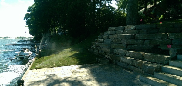 A large block stone retaining wall is used to deal with a steep slope down to the lower patio area and the dock on this cottage property.