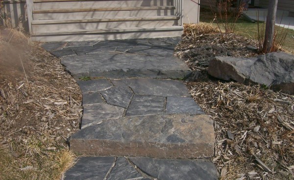 A rustic dry laid flagstone walkway welcomes people to this modern home in the city. Instead of sloping a walkway, incorporate a few stone slab steps as seen in this picture.