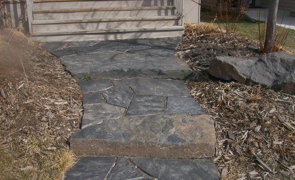 A rustic dry laid flagstone walkway welcomes people to this modern home in the city. Instead of sloping a walkway, incorporate a few stone slab steps as seen in this picture.