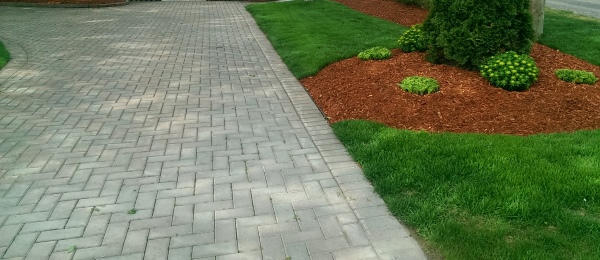 A brick paver driveway is contrasted by red mulch and a deep green lawn. This is a very simple and affordable low maintenance front yard idea.