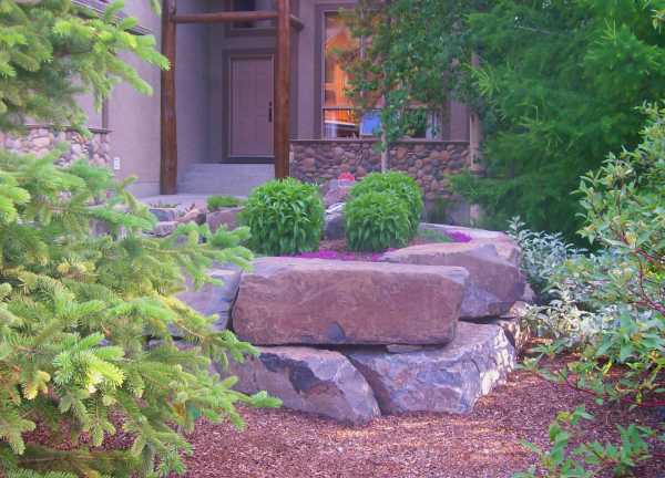 A large block stone retaining wall extends the entryway to include a small garden bed in this front yard.
