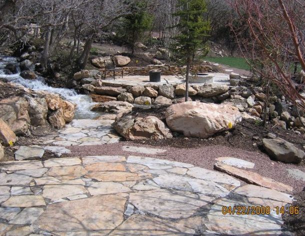 Two patios are connected by a flagstone walkway and large boulders placed in the stream.