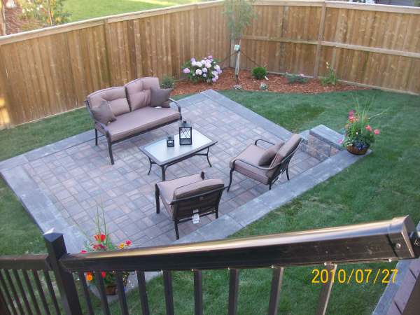 Formal manufactured brick patio recessed into a slope in a small backyard.