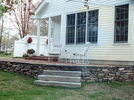 A rustic looking stone wall supports a walkout patio area. 