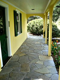 Flagstone porch patio bordered with a garden bed in front leads out to the side yard.