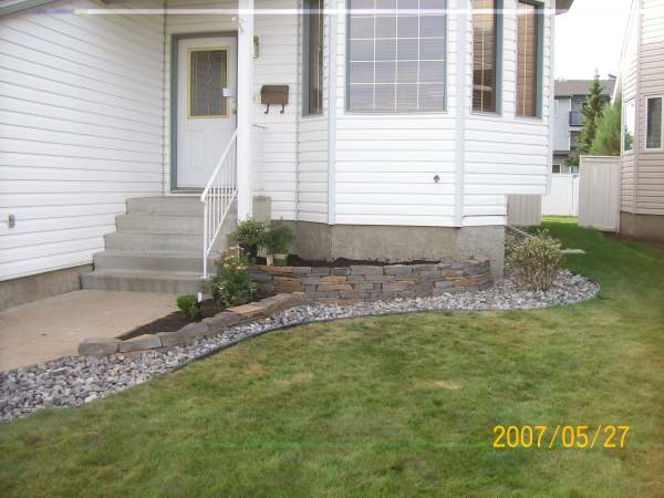 A small front garden bed made with natural stone dresses up the front yard while hiding the concrete foundation.