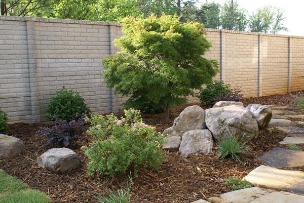 A bed with small shrubs and rocks complimenting the main feature that stands tall in the center.