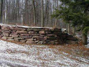 A dry-stacked fieldstone wall in the winter. This curved wall adds some