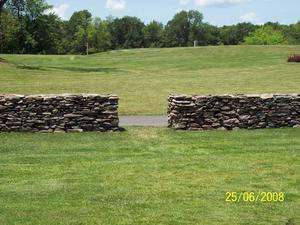 A free standing dry-stacked stone wall with an open gateway.