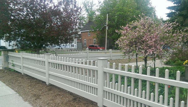 A modern picket style fence provides an attractive barricade for this corner lot. Manufactured block pillars sit on each corner.