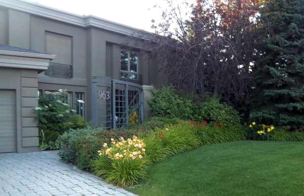 A formal looking home is transformed by this informal front garden. The soft flowing curve with mixed grasses, perennials, and shrubs creates a