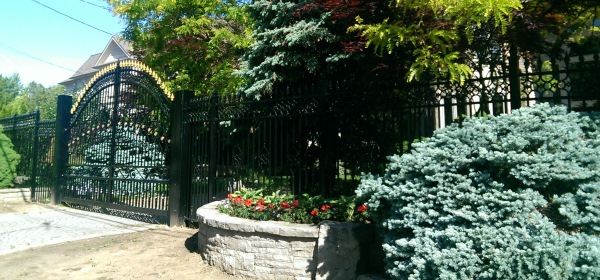 A wrought iron fence combined with some trees and a raised stone garden bed  provide an elegant look to this secured residence.